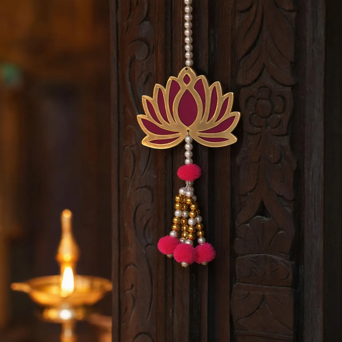 A gold mirror lotus latkan on a carved door beside a lit diya